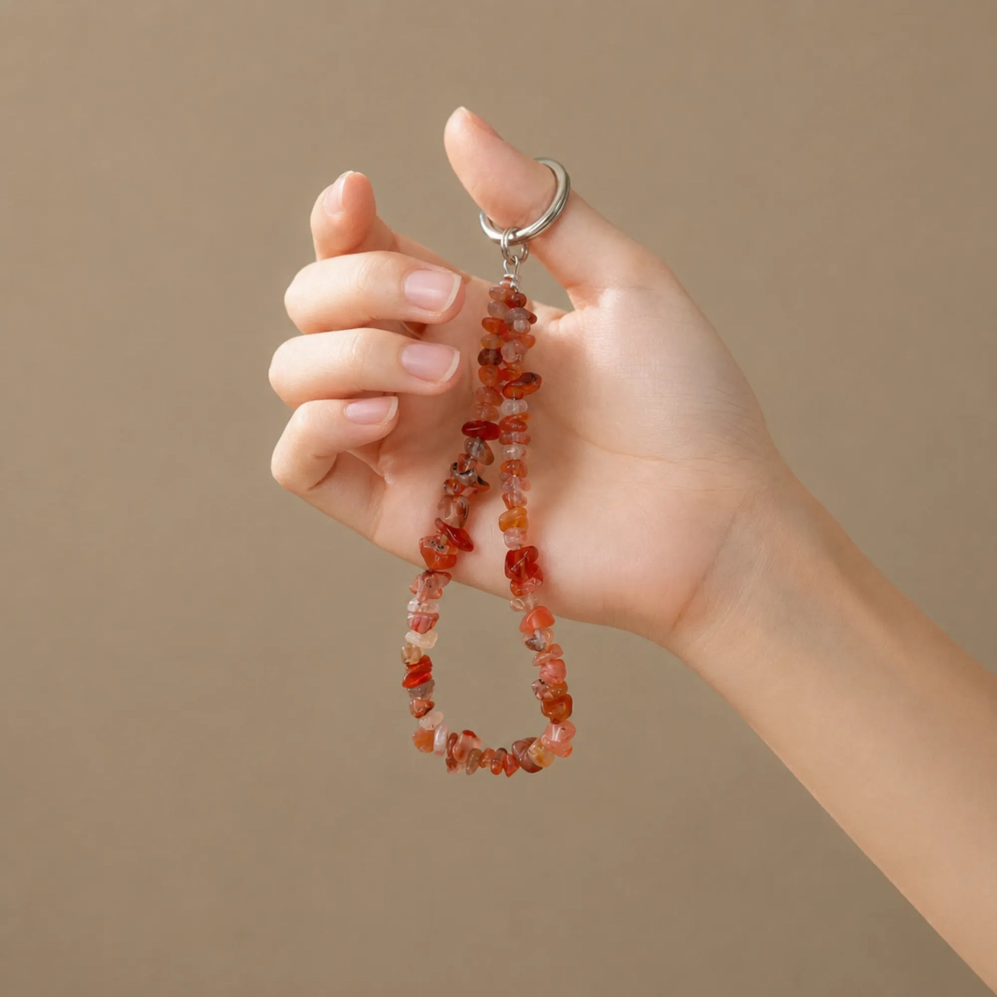 Hand holding a red agate chip phone charm
