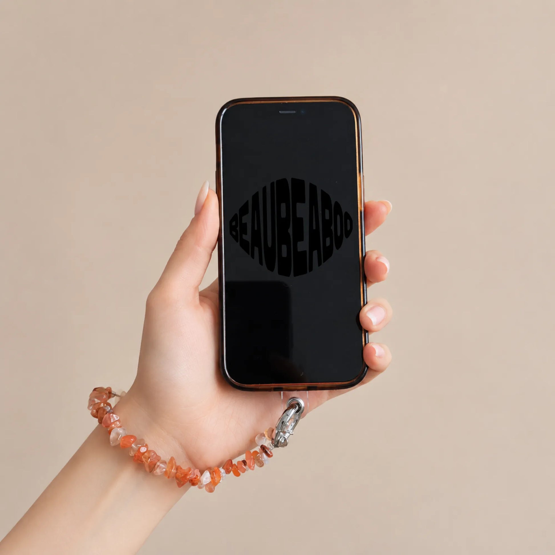 Hand holding a phone with a red agate chip phone charm