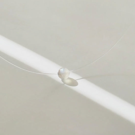 Collier à perle flottante en pierre grise, à la lumière du soleil, en mouvement.