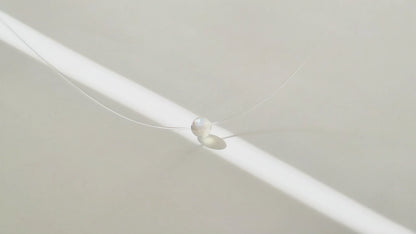 Collier à perle flottante en pierre grise, à la lumière du soleil, en mouvement.