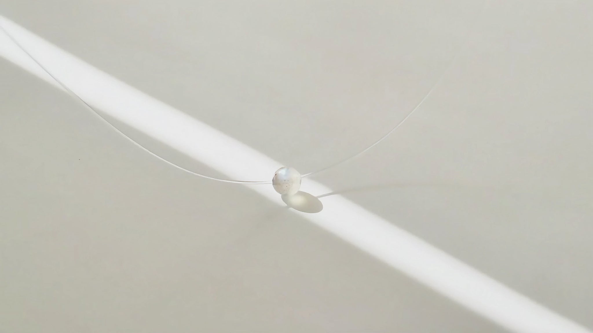 Collier à perle flottante en pierre grise, à la lumière du soleil, en mouvement.